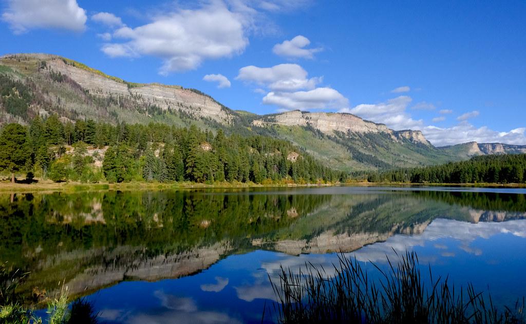 A tranquil lake perfectly reflects mountains, trees, and a bright blue sky.