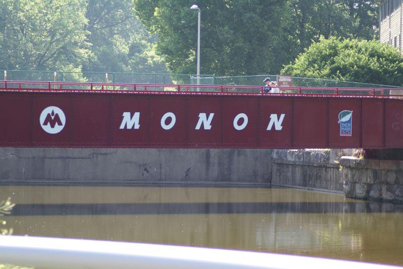 Red metal bridge with white letters over water, people walking on top.