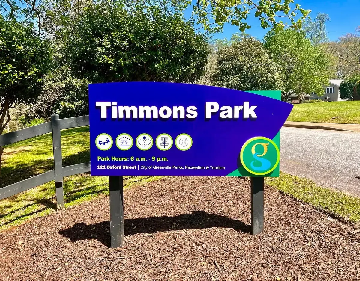 Blue park sign with white text and activity icons under bright sunlight.