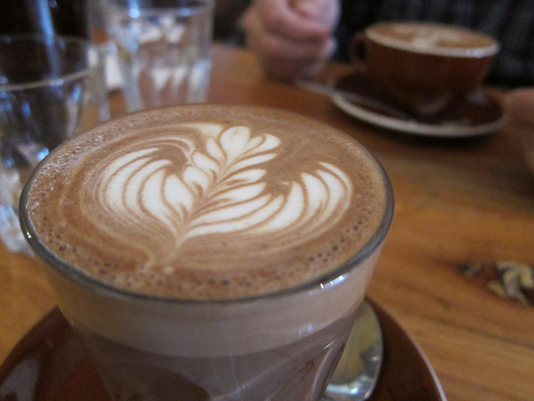 Warm latte with detailed foam art on a wooden table, soft light.