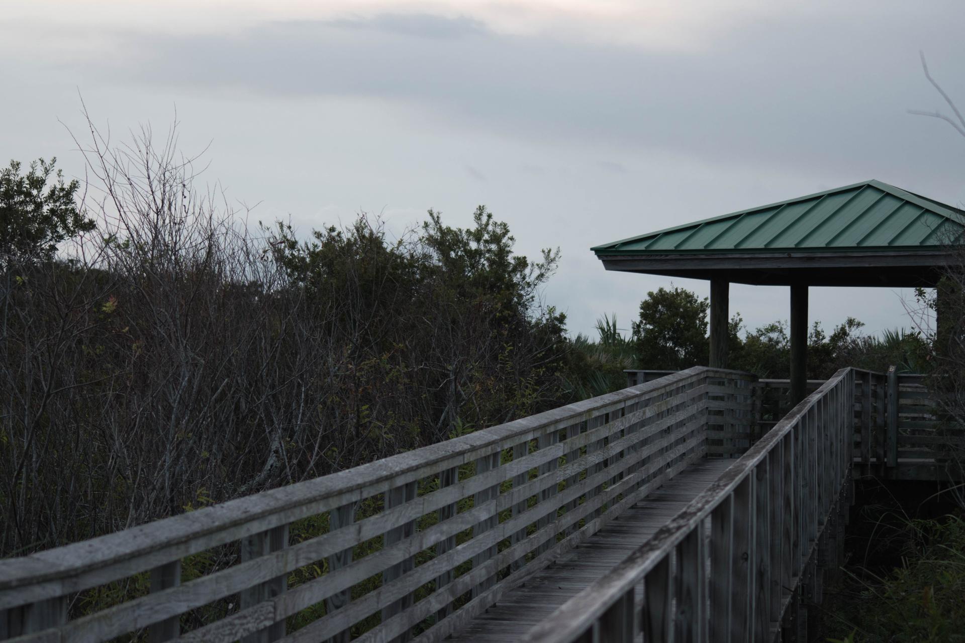 A wooden boardwalk leads to a green-roofed gazebo under an overcast sky.