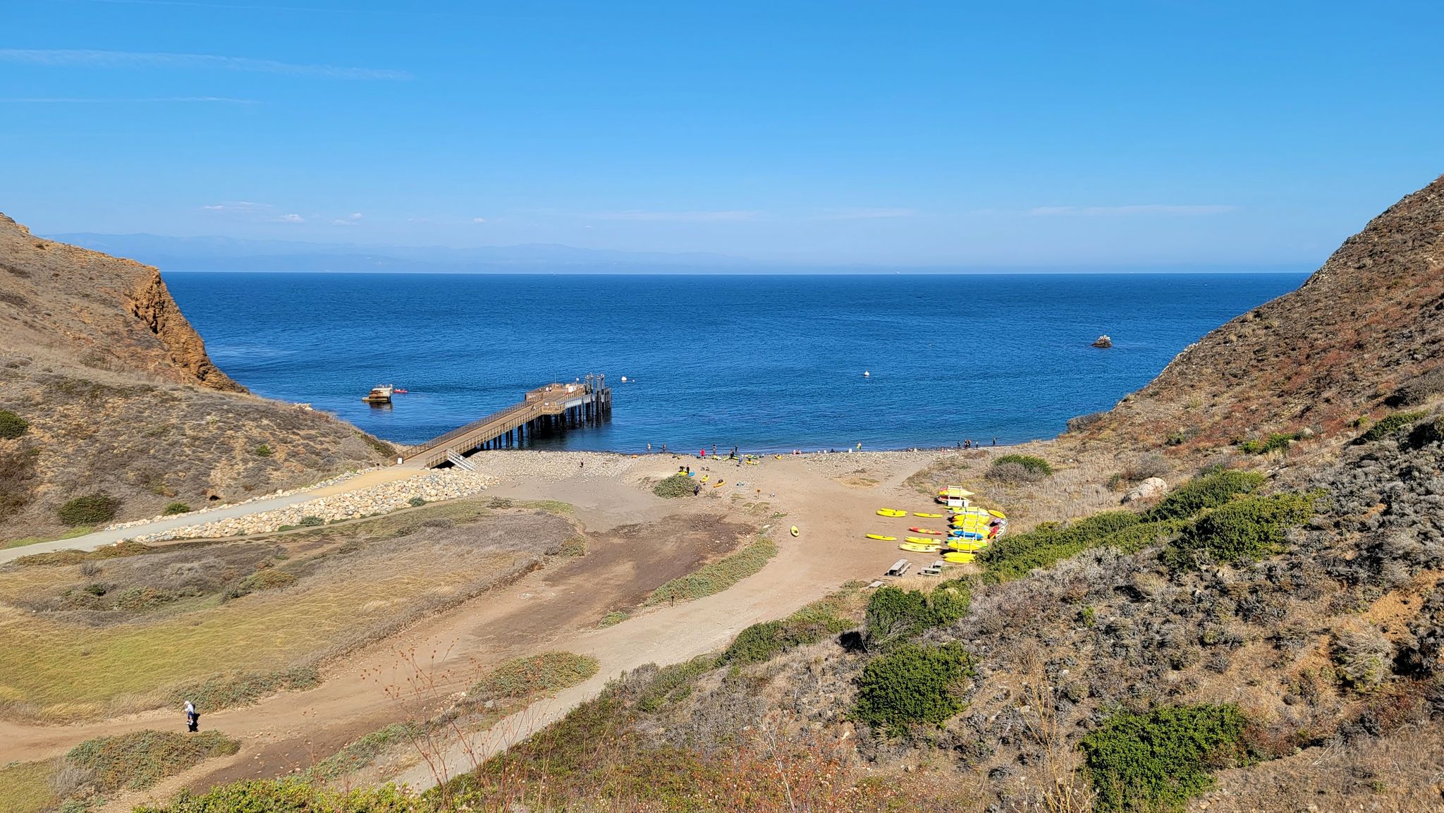 Sunny cove with a pier, blue ocean, and kayaks on a sandy beach. - Scorpion Canyon Loop Trail