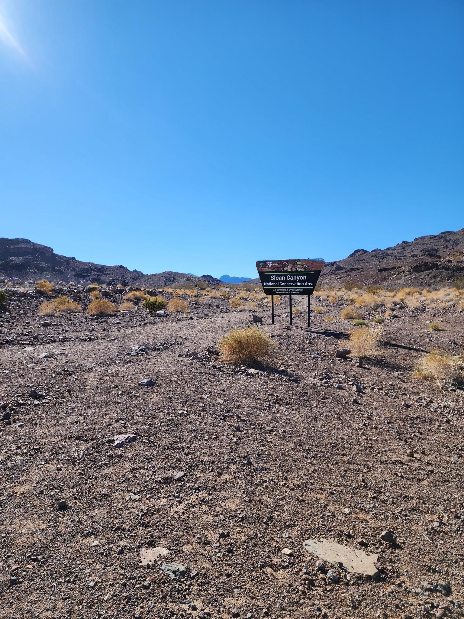 An information sign stands on a dirt path in a bright, arid desert landscape. - 601 Trail to 701 Trail Loop