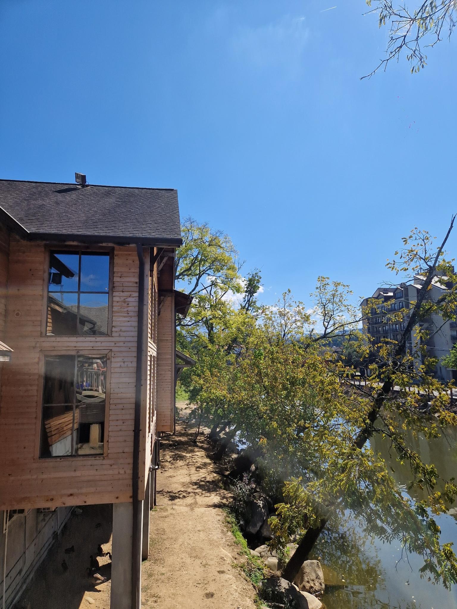 Wooden building next to a river with green trees under a bright blue sky.