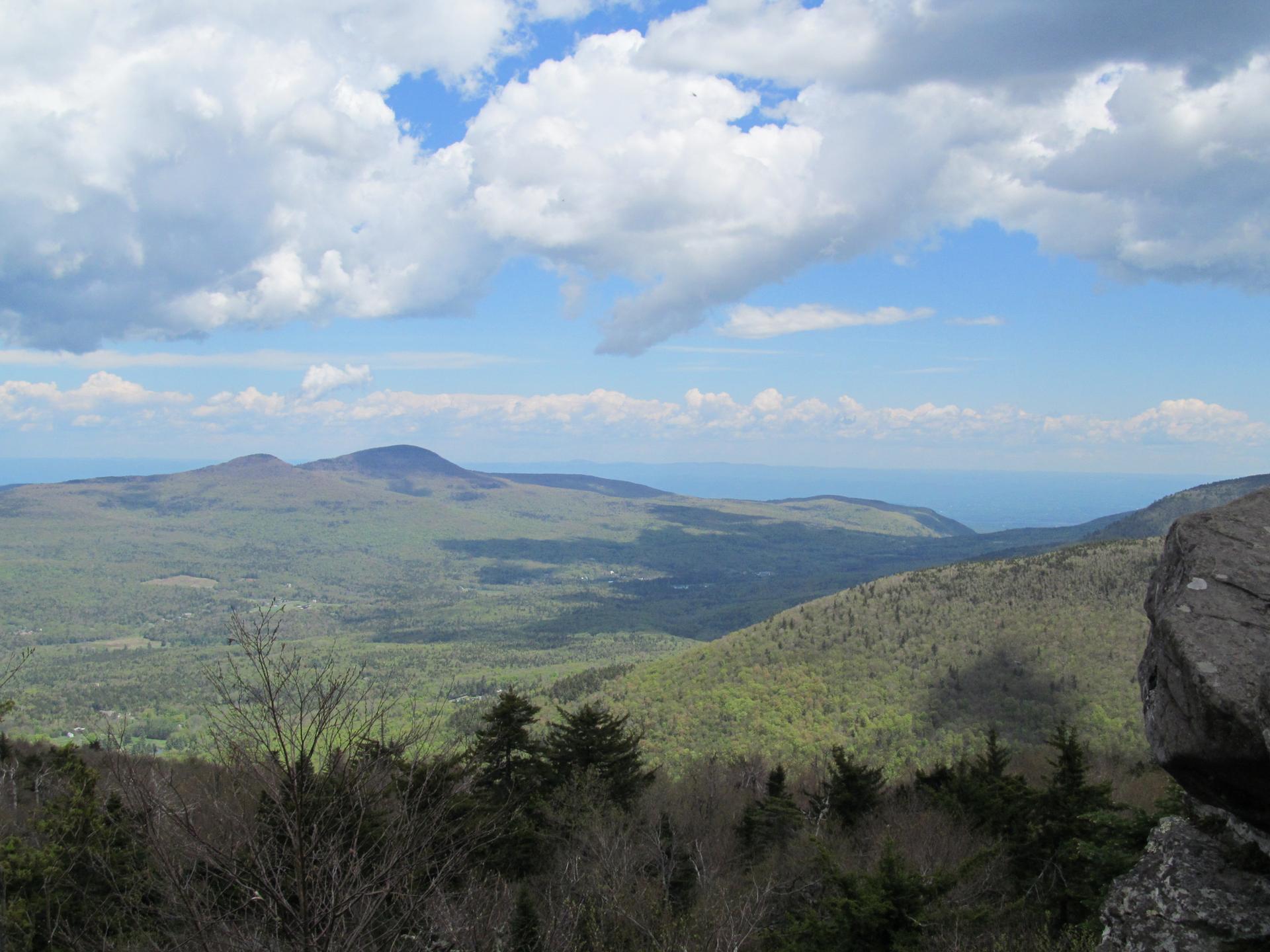 Panoramic view of forested mountains under a bright, partly cloudy sky.