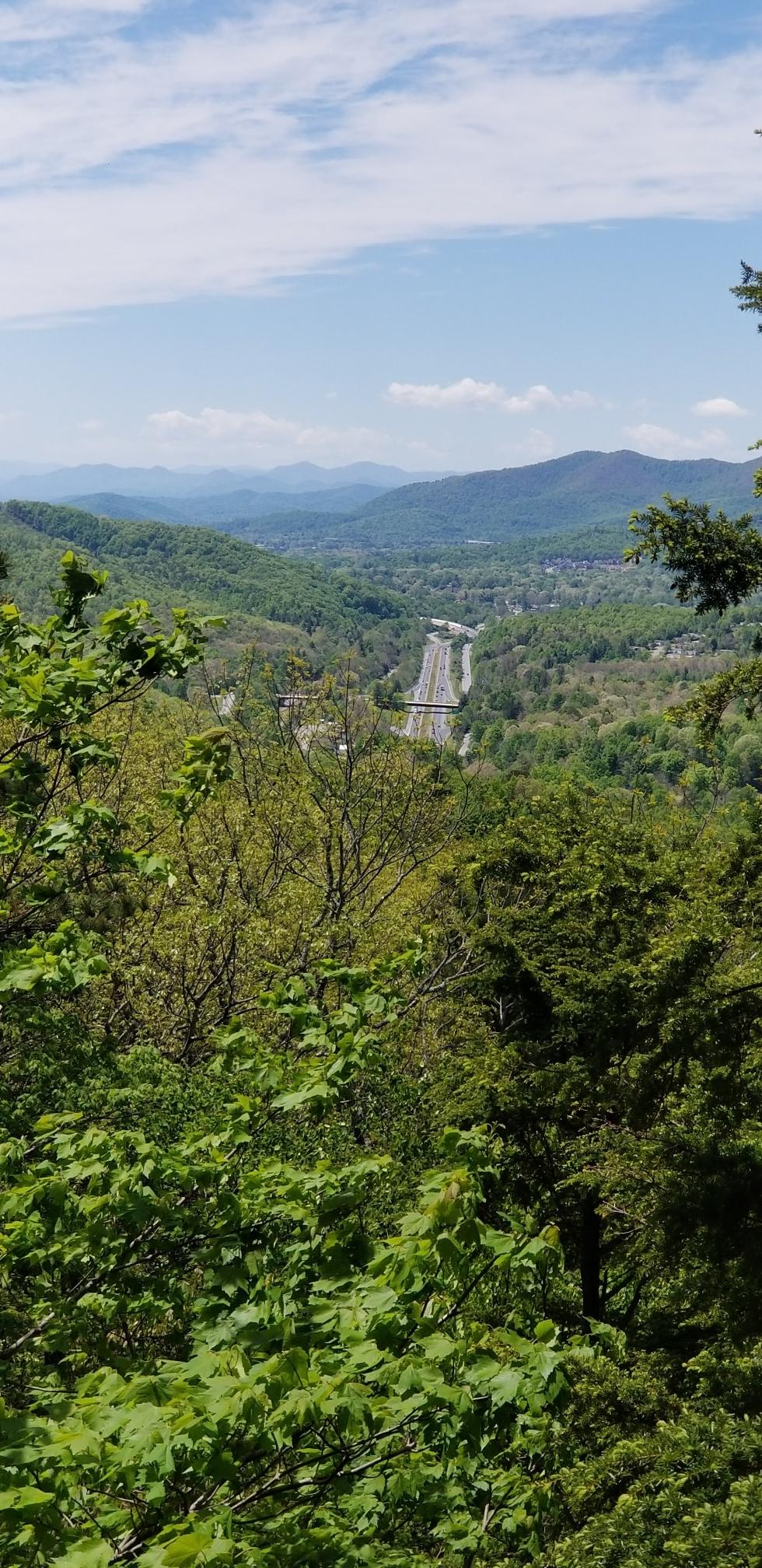 Panoramic view of a valley with a highway, surrounded by green mountains.
