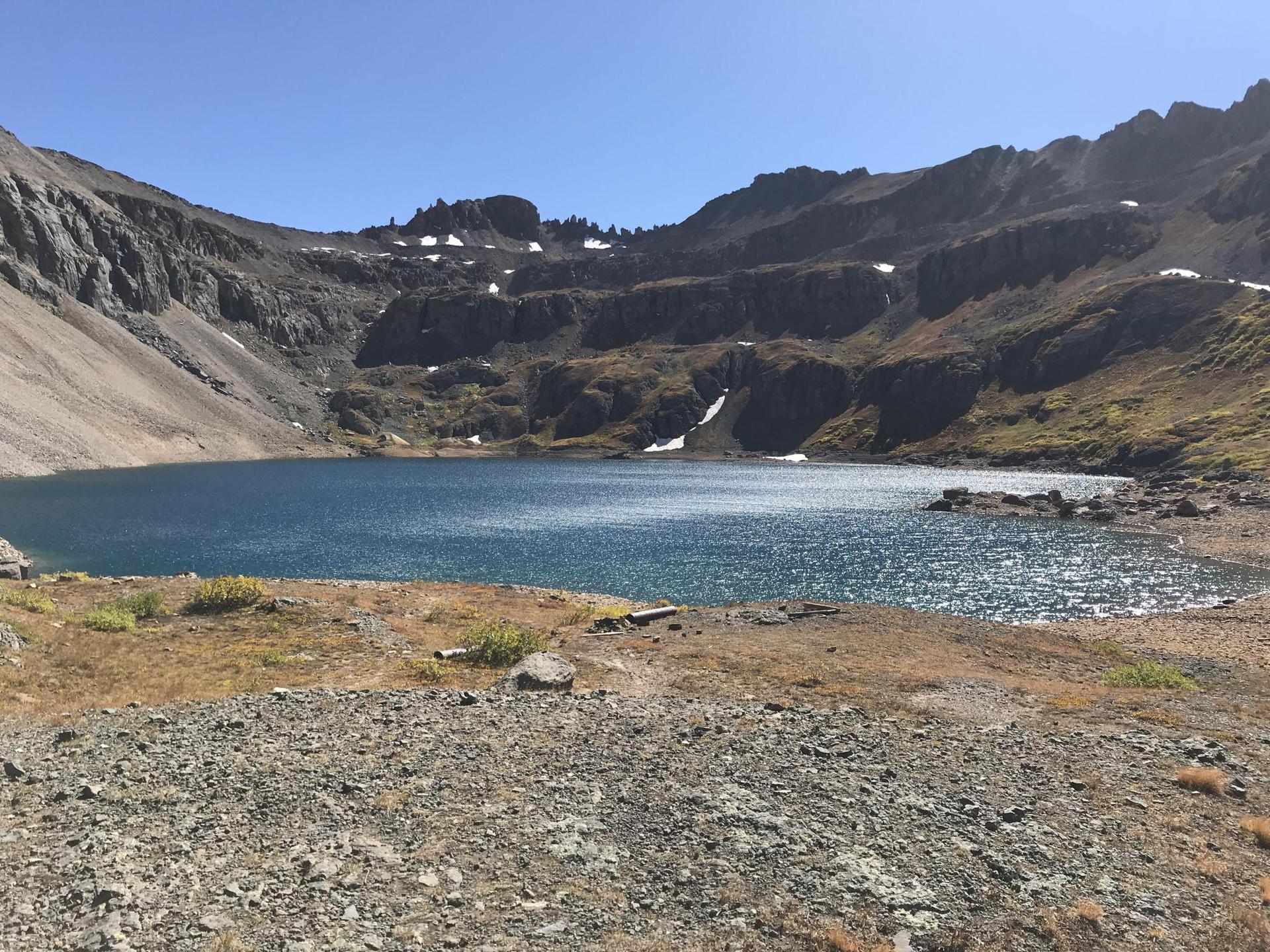 Blue alpine lake surrounded by rocky, snow-dusted mountains under clear skies.