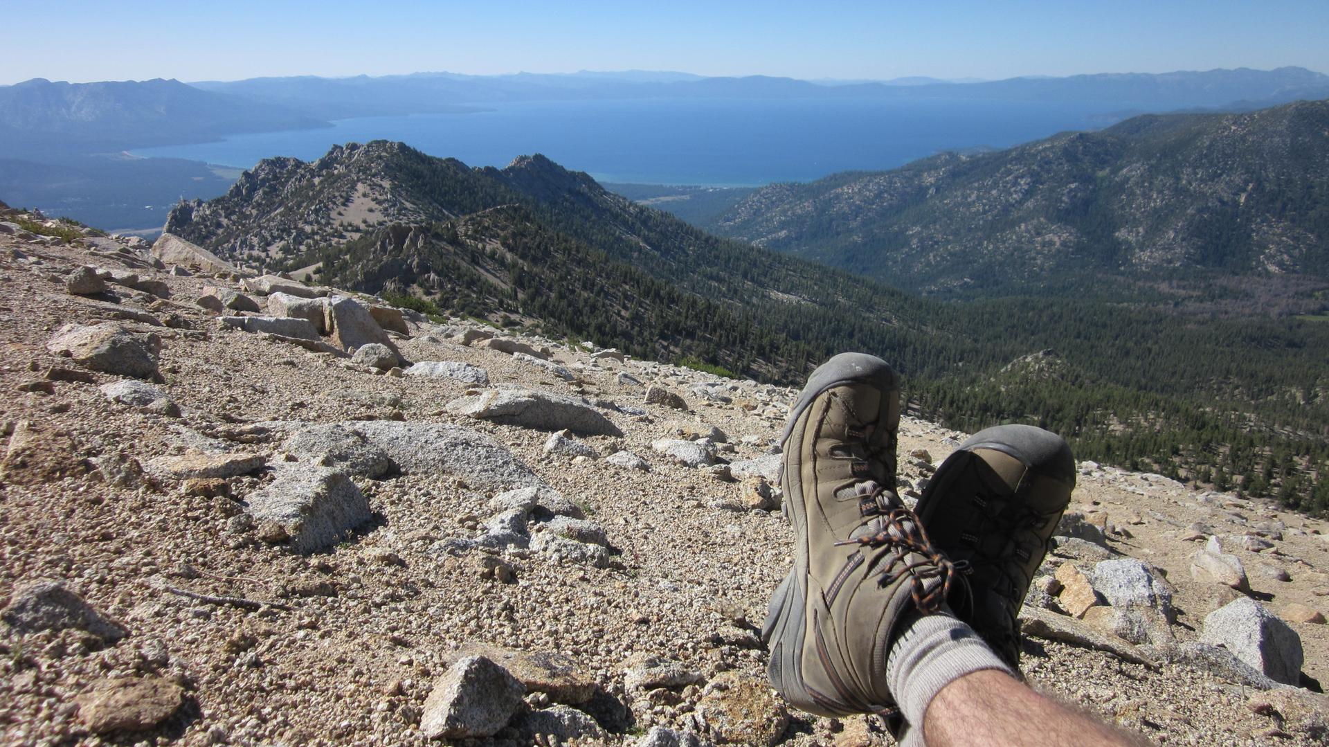 Hiker's boots resting on a rocky mountain peak overlooking a vast lake.