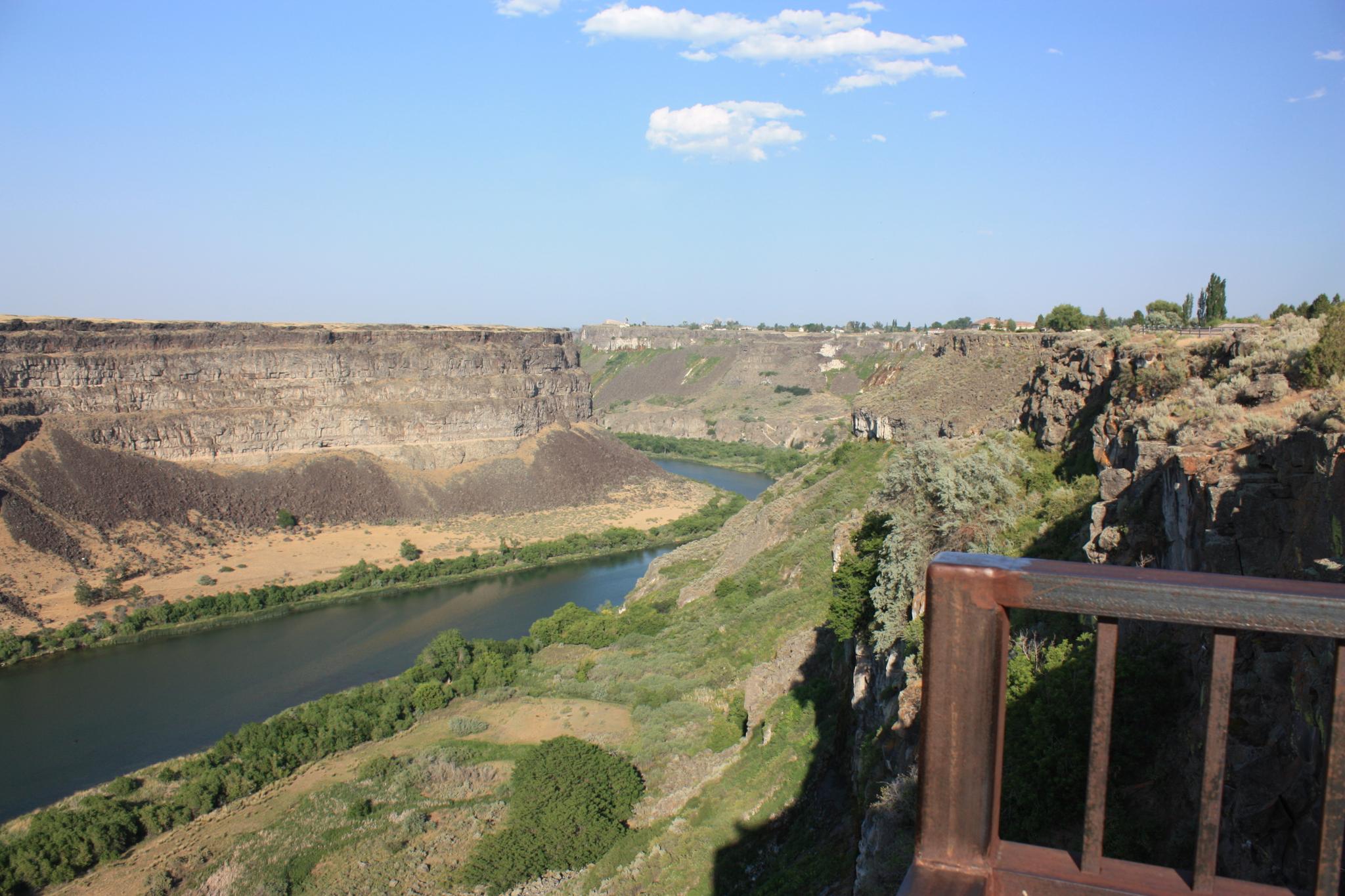 Scenic canyon view with a river and distant bridge under a blue sky.
