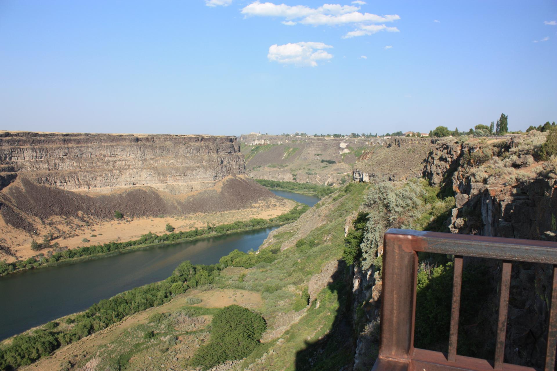 Scenic canyon view with a river and distant bridge under a blue sky.