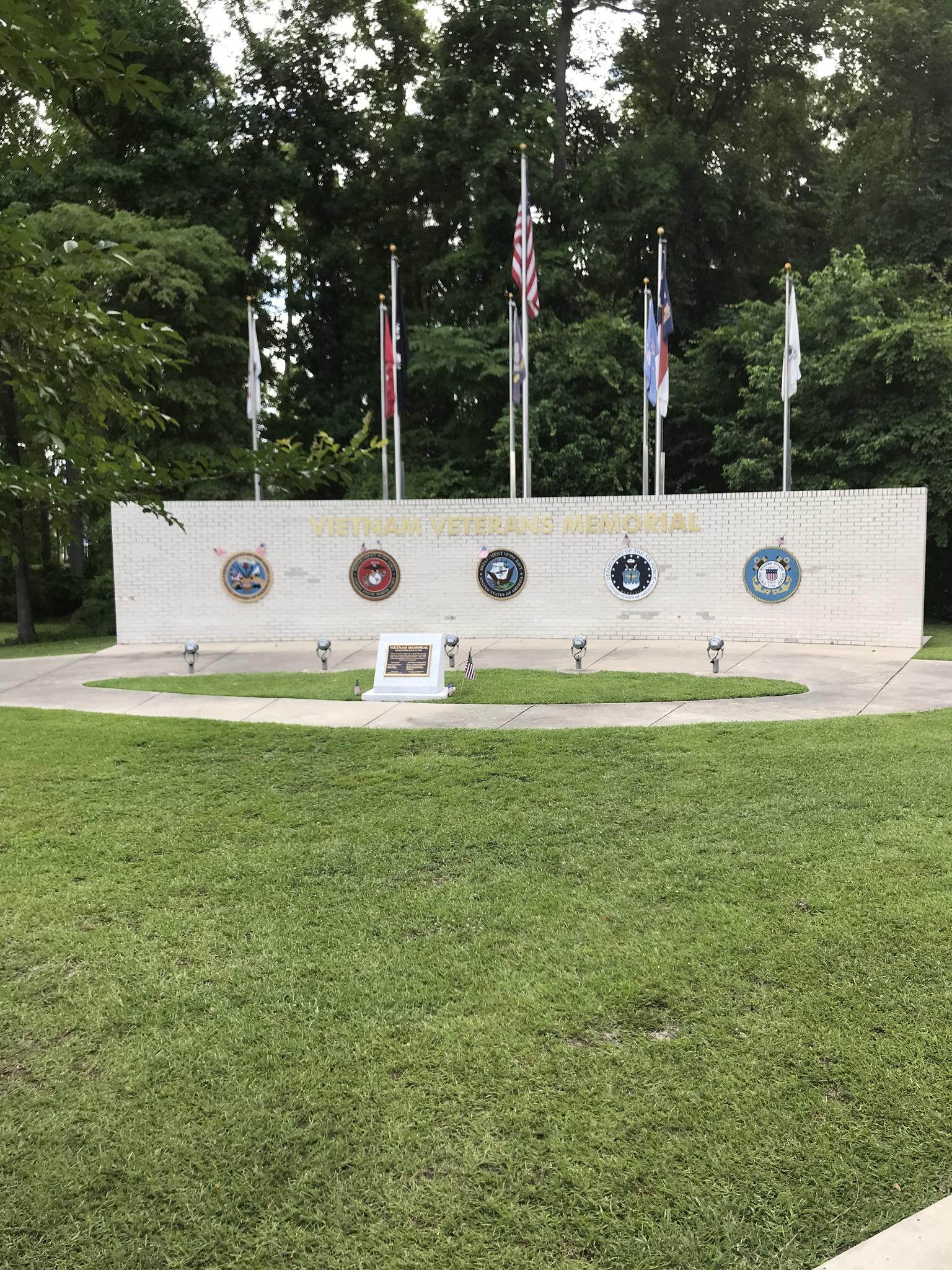 Memorial wall with flags and emblems on a grassy lawn.