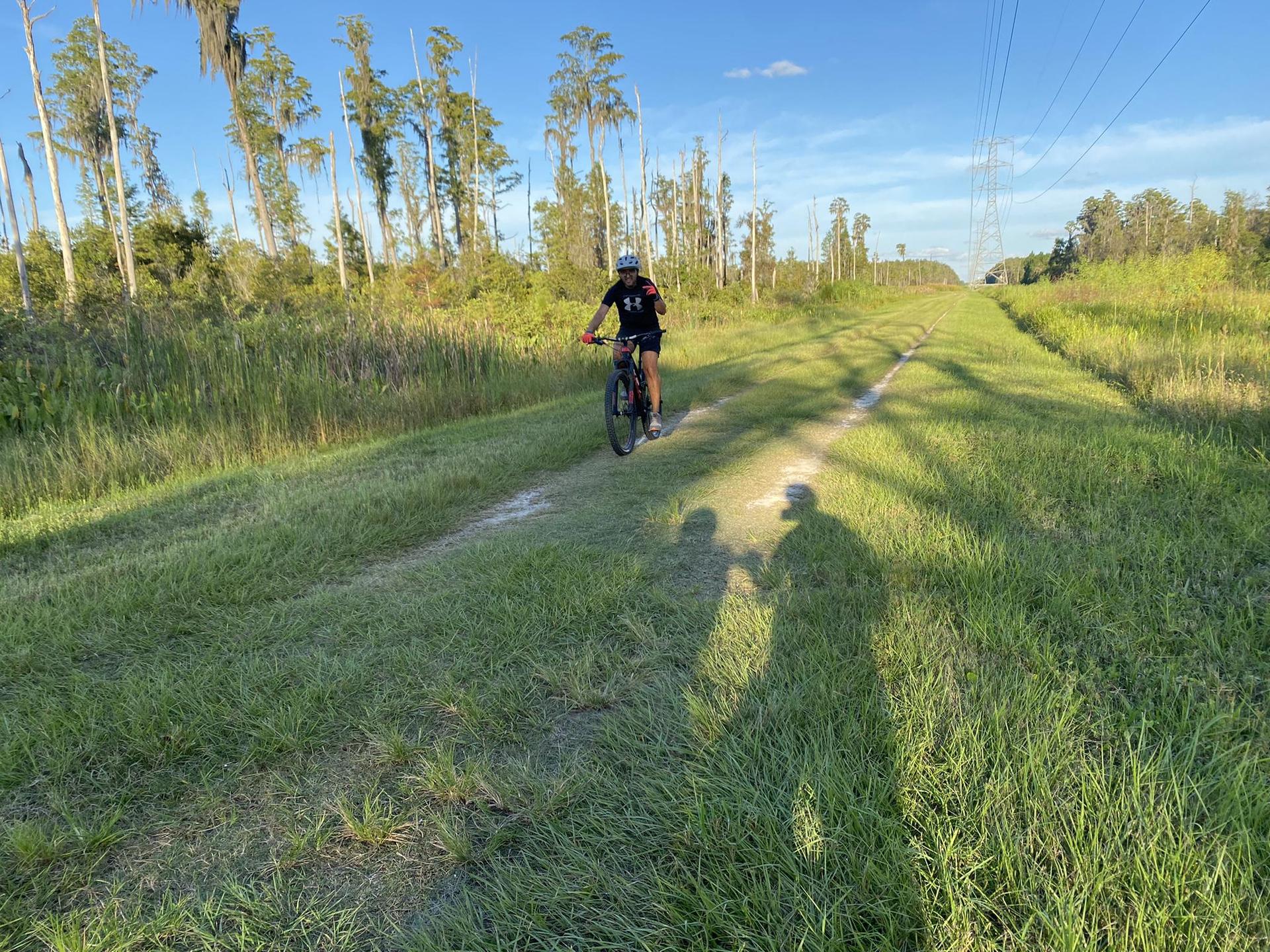 A person cycles on a grassy path, casting long shadows in golden light.