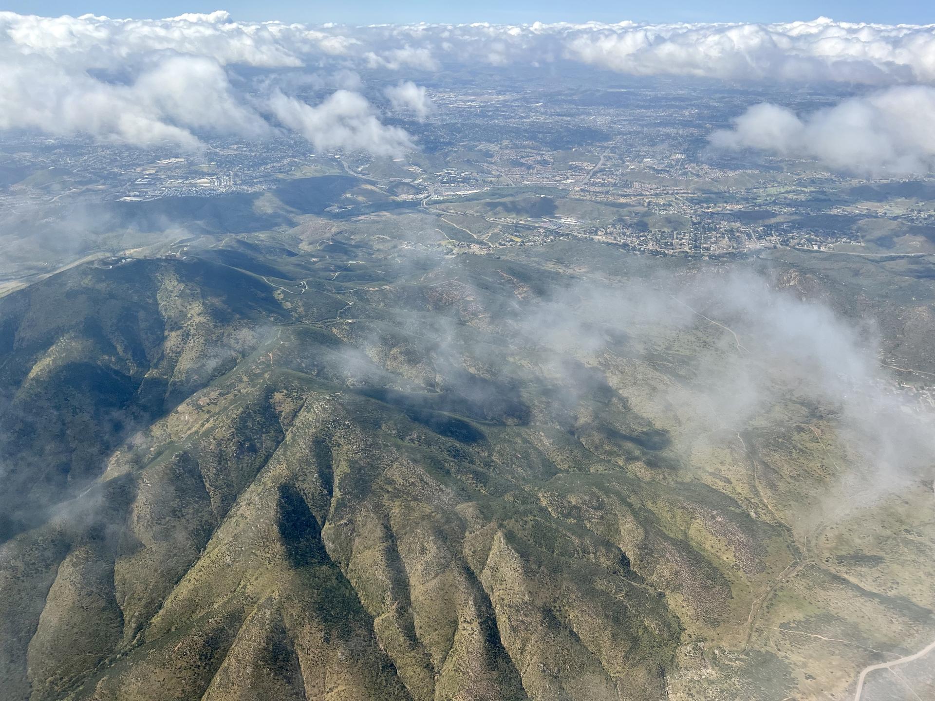 Aerial view of green mountains and valleys partially covered by clouds, with a distant town.