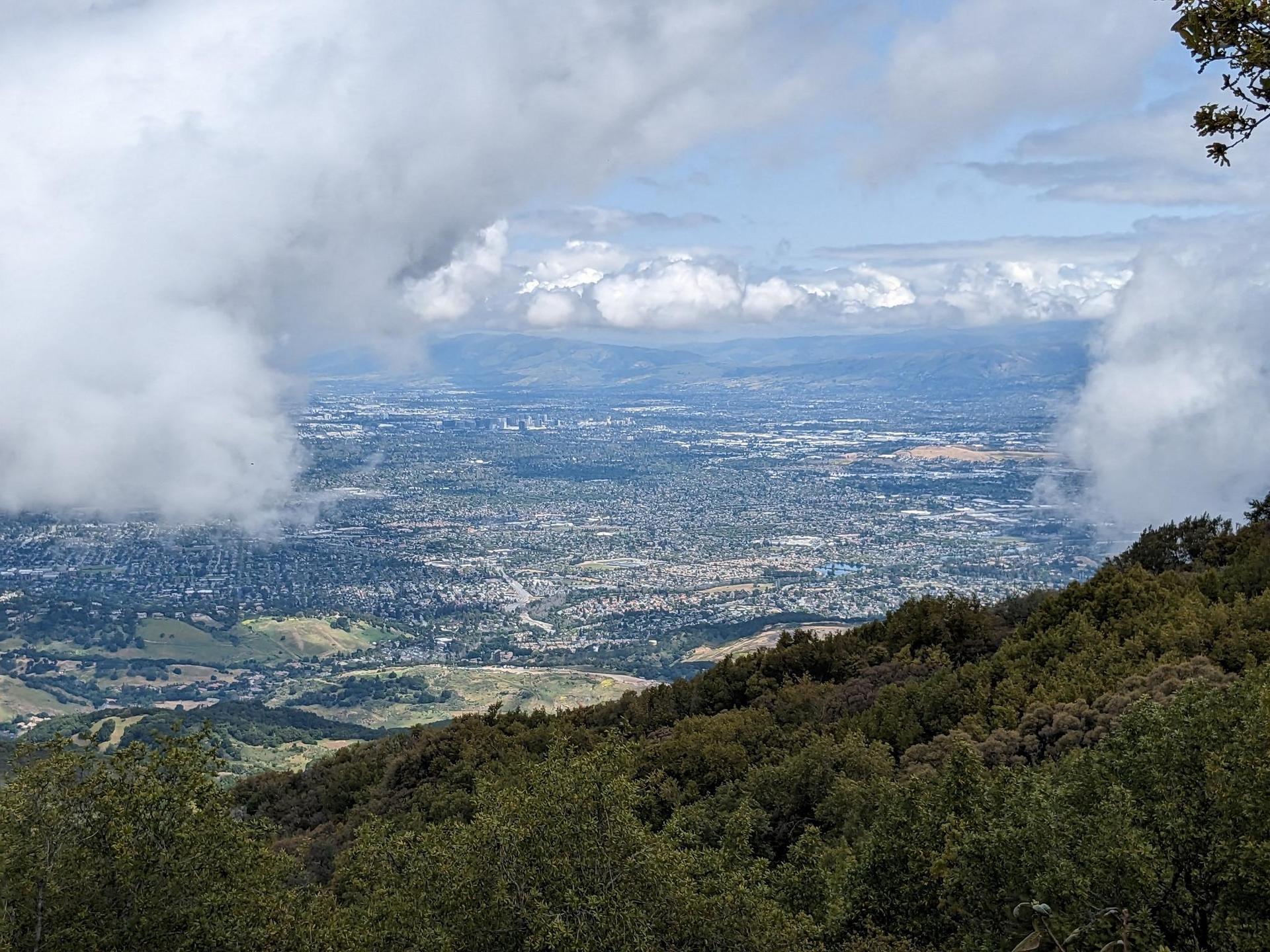 A vast city view from a mountain, partially covered by white clouds.