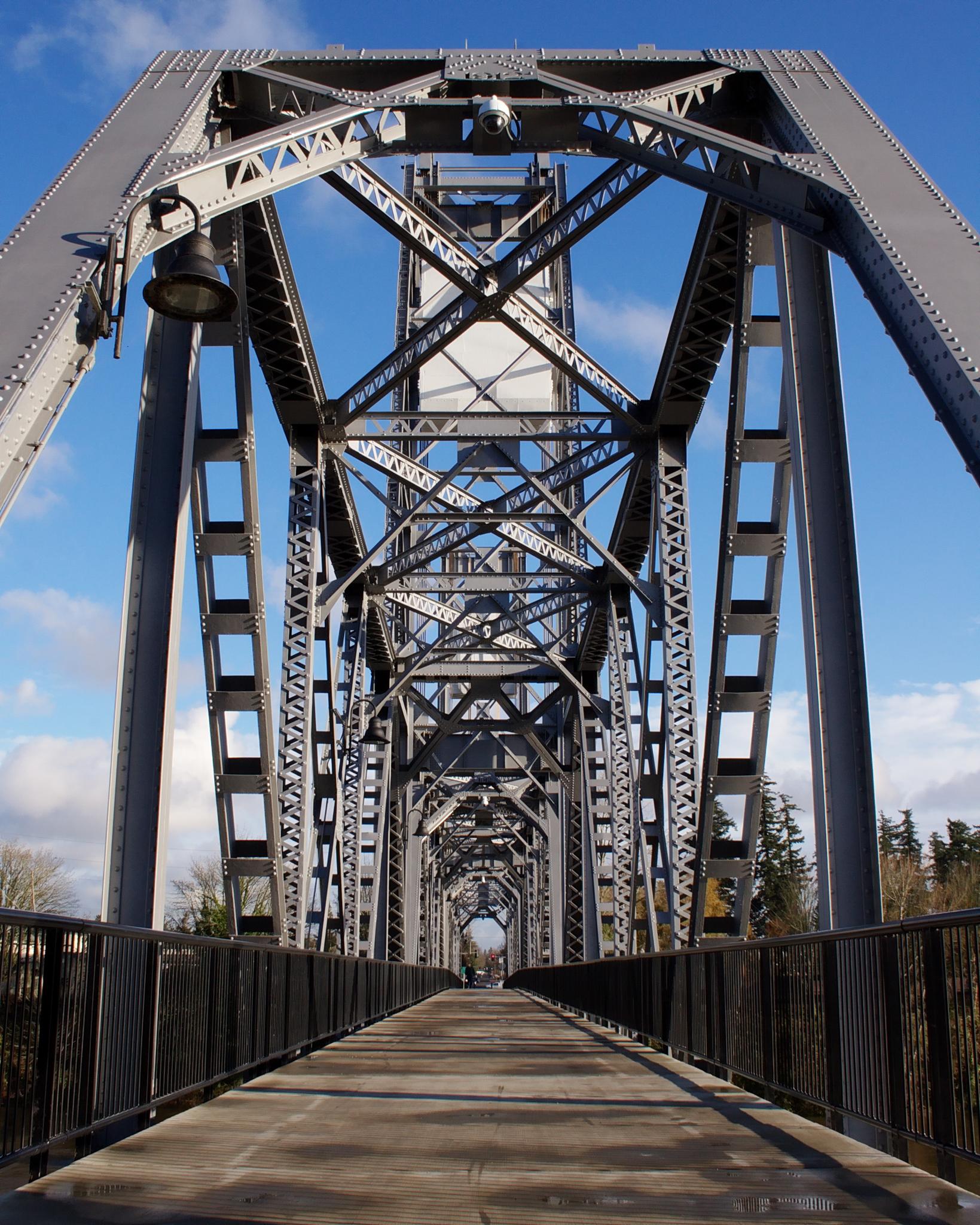 Symmetrical view of a large, intricate metal bridge structure on a sunny day.