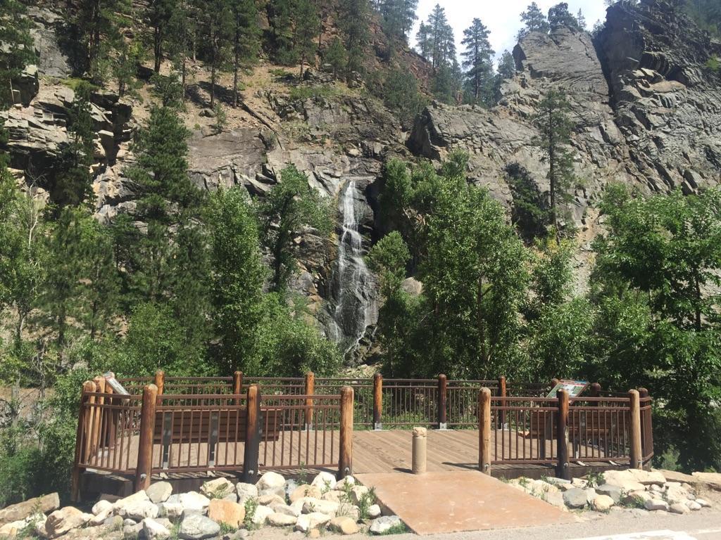 Waterfall cascading down a rocky cliff, viewed from a wooden platform.