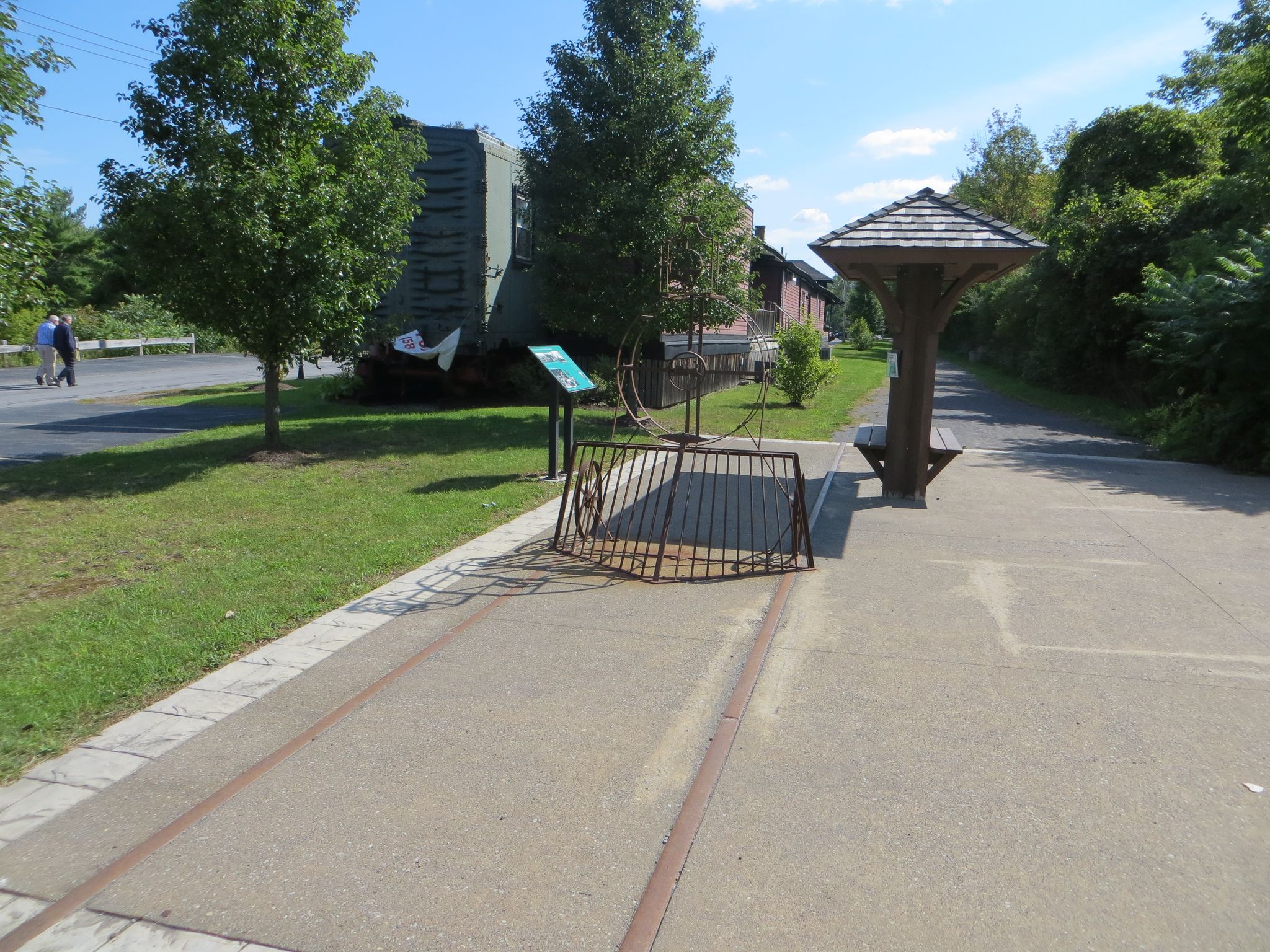 Paved path with embedded tracks, a shelter, and distant walkers on a sunny day. - Auburn Trail