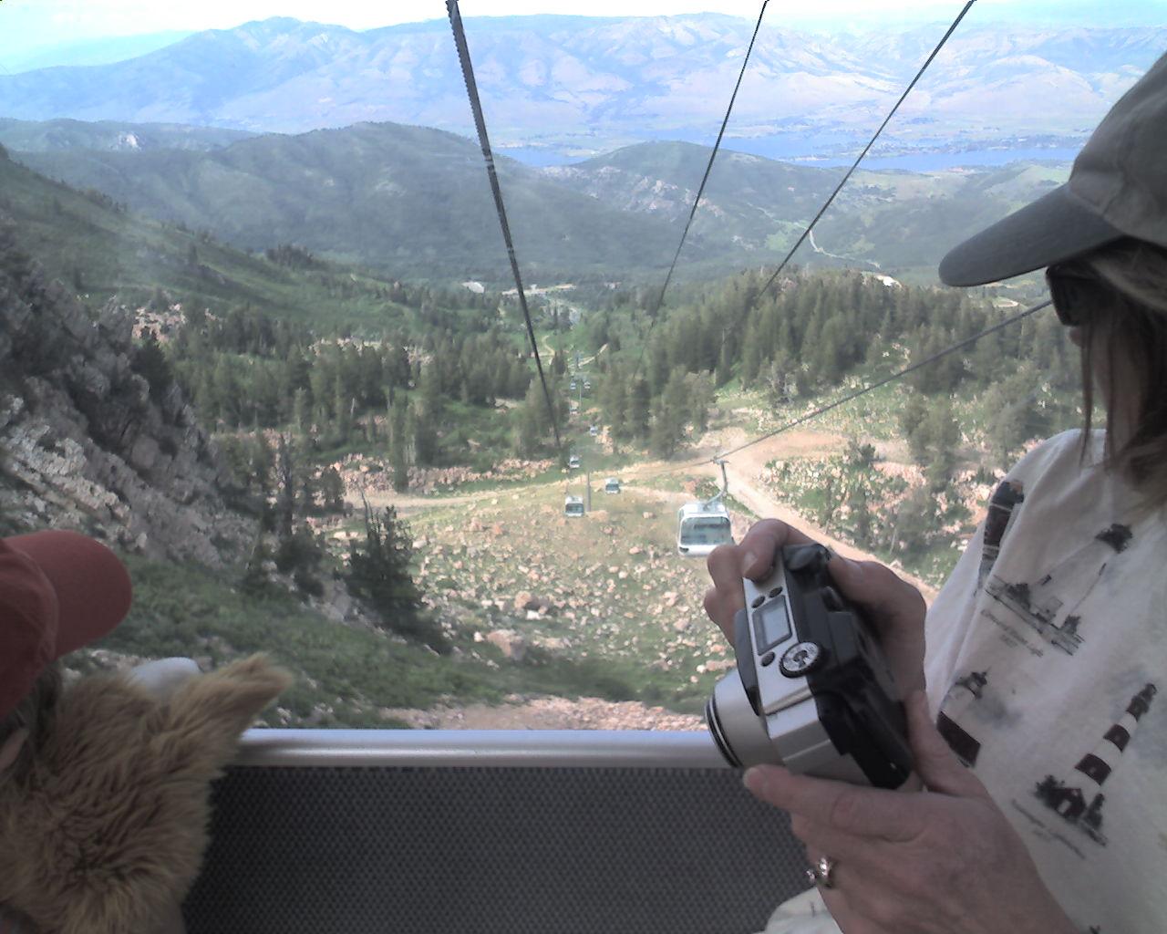 Person in gondola holds camera, overlooking a vast mountain valley.