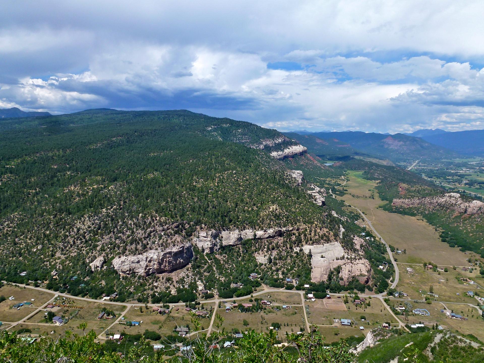 Aerial view of forested mountains, rocky cliffs, and a valley with homes.