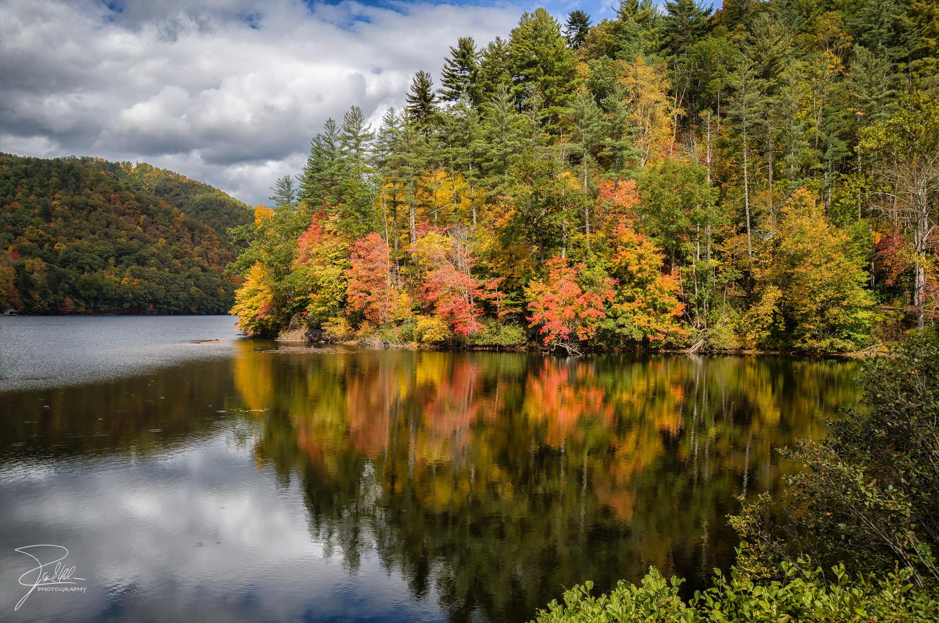 Calm lake reflecting vibrant autumn trees under a cloudy sky.