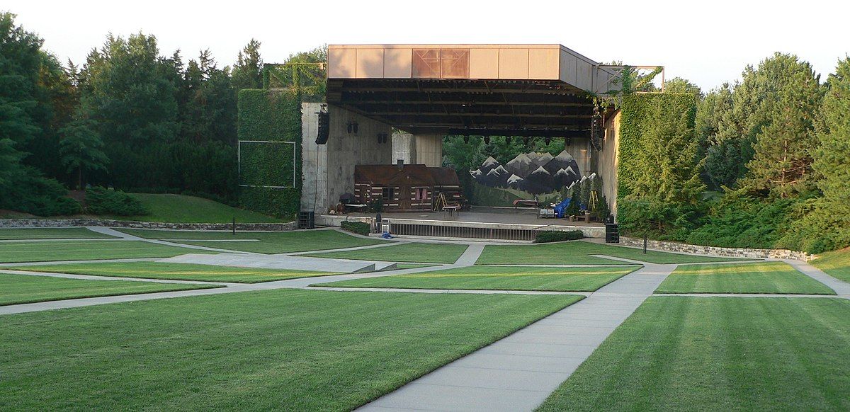 Empty outdoor amphitheater stage with a large grassy lawn. - Prairie Corridor Trail