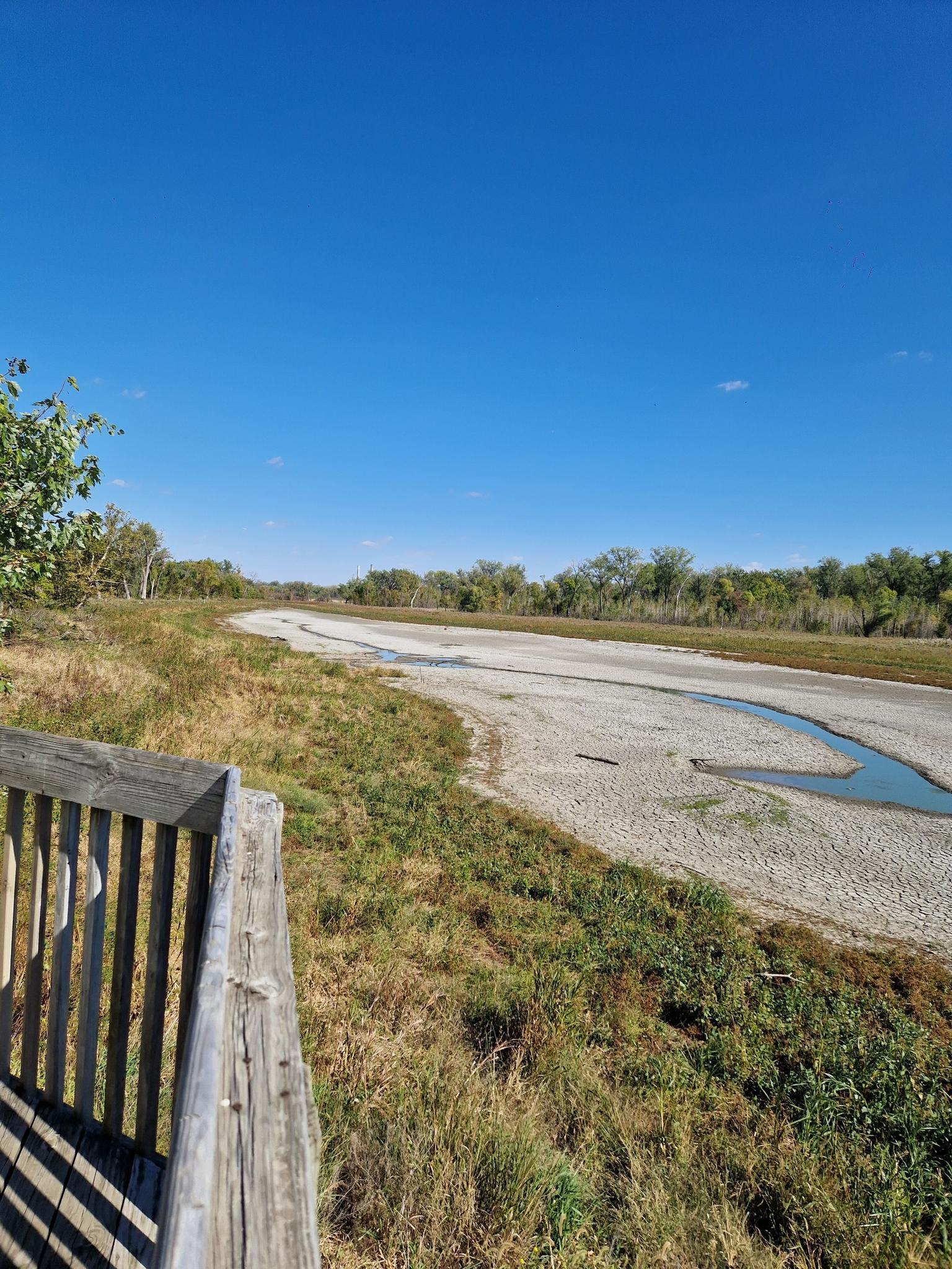 Sunny view of a dry riverbed with a small stream, from a wooden platform.