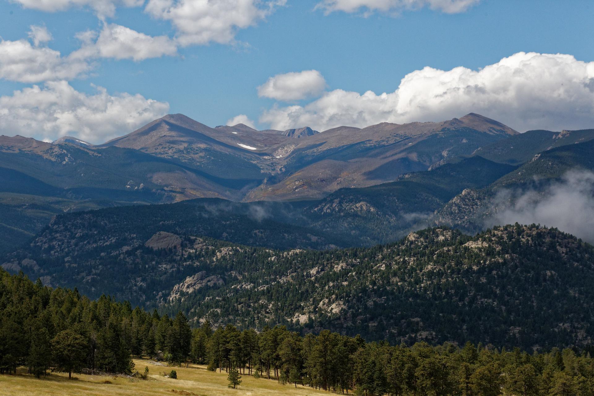 Majestic mountains with dark forests and clouds under a partly cloudy sky.