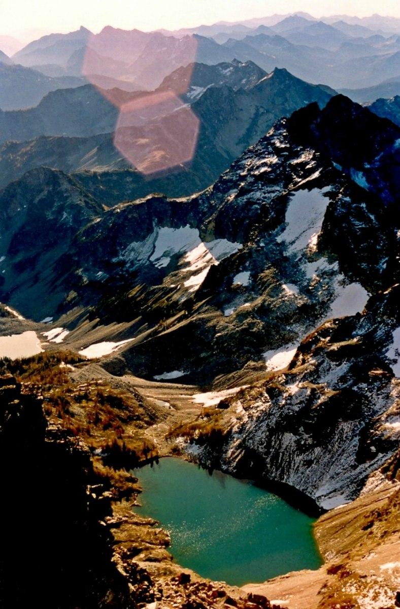 Aerial view of a turquoise mountain lake and snowy peaks at sunset.