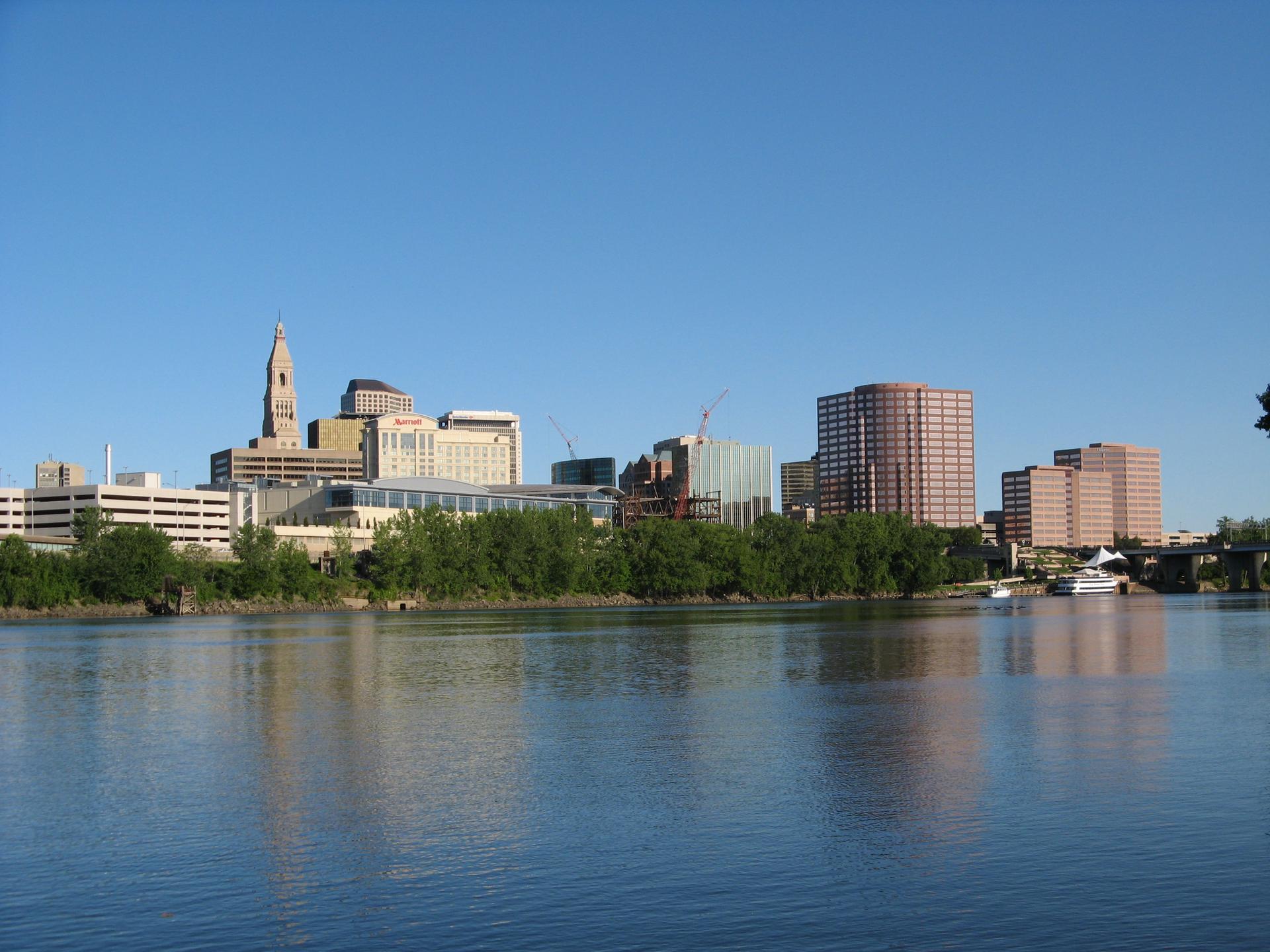 City skyline with tall buildings reflected on a wide river.