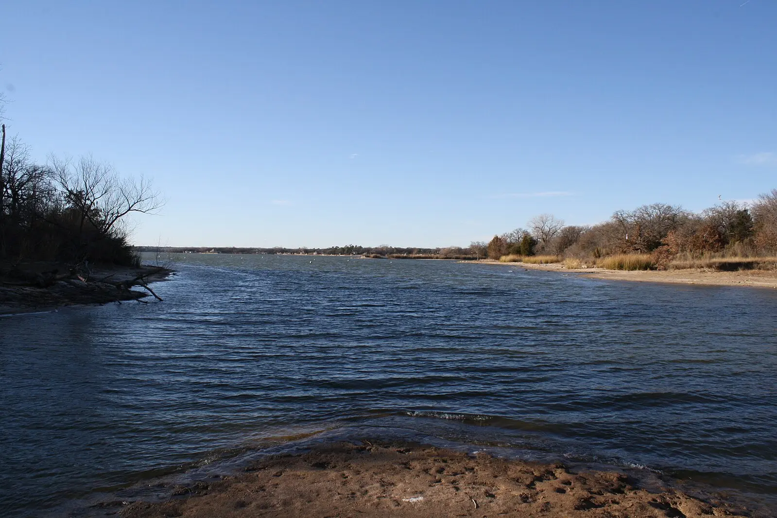 Rippling blue water flowing between wooded banks on a sunny day.