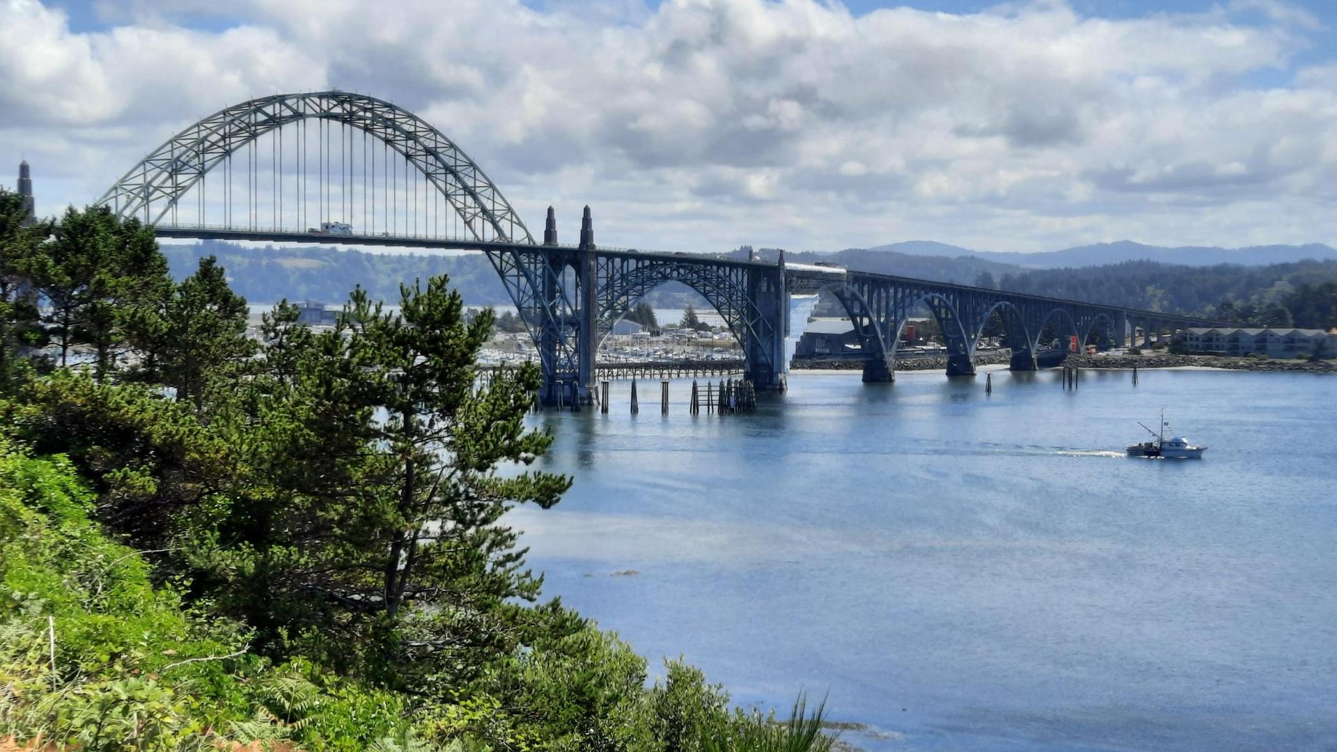 Arched bridge over water with a boat, surrounded by green trees and hills.