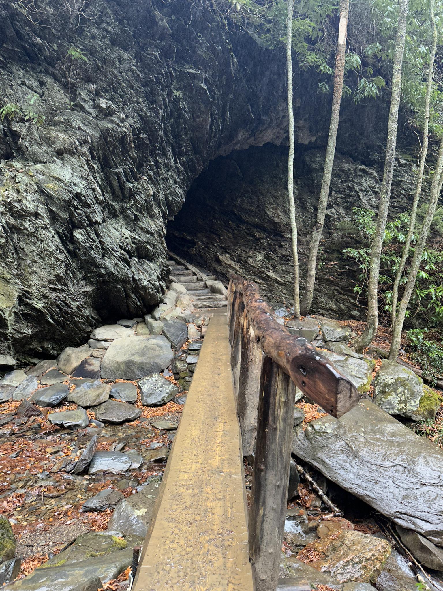 Wooden walkway and stone steps lead into a dark rock cave.