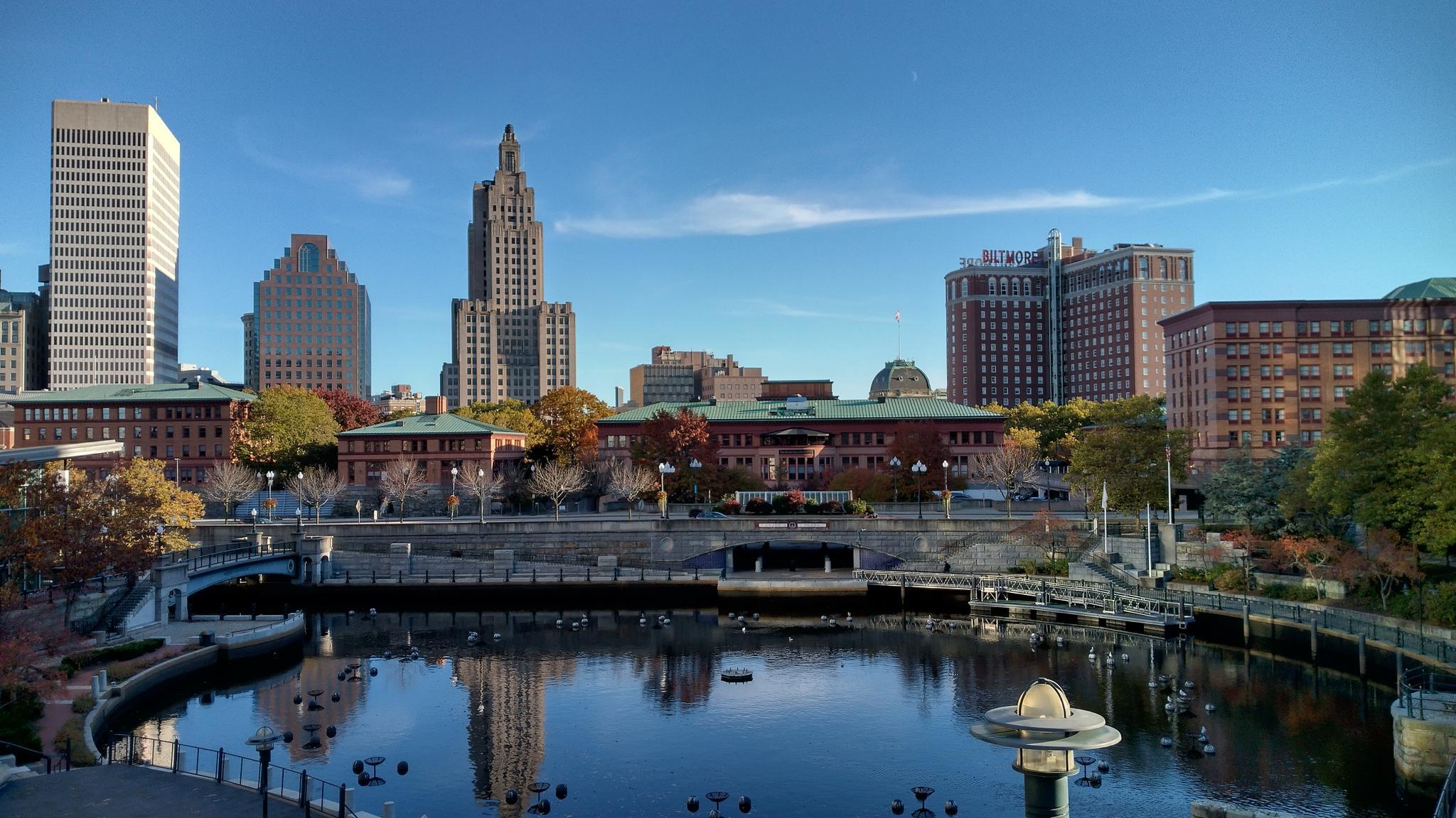 City skyline with tall buildings reflecting in calm water on a clear day.