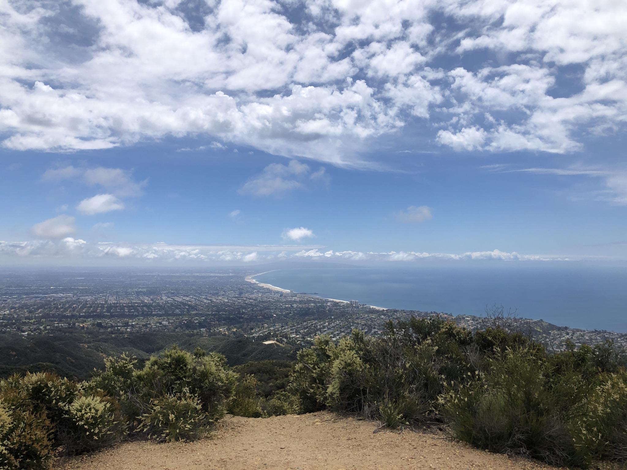 Panoramic view of a coastal city and ocean under a cloudy blue sky.