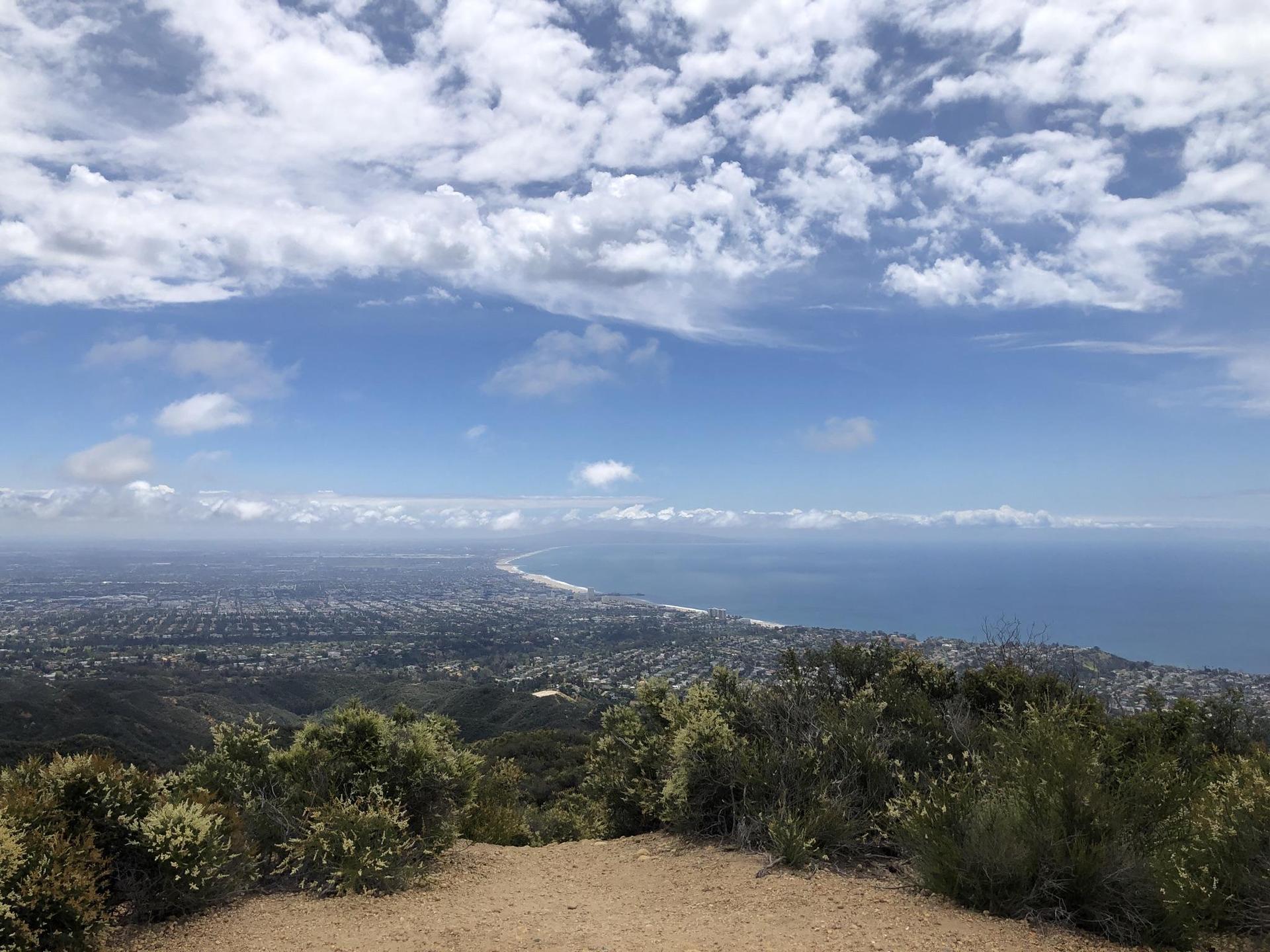 Panoramic view of a coastal city and ocean under a cloudy blue sky.
