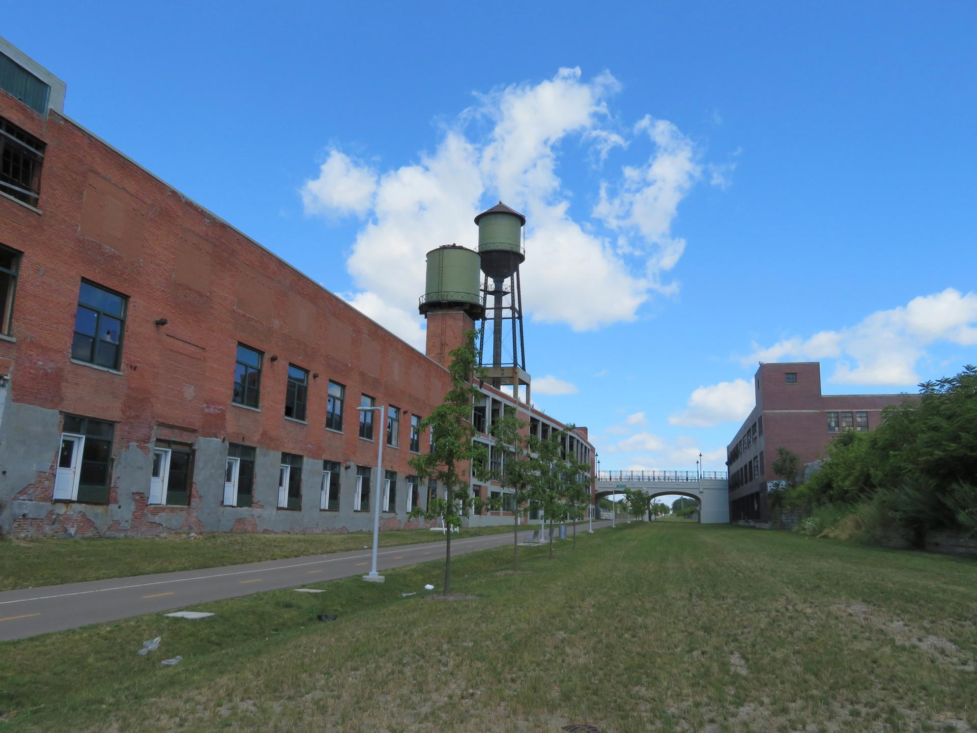 Old brick industrial buildings alongside a grassy path under a blue sky.
