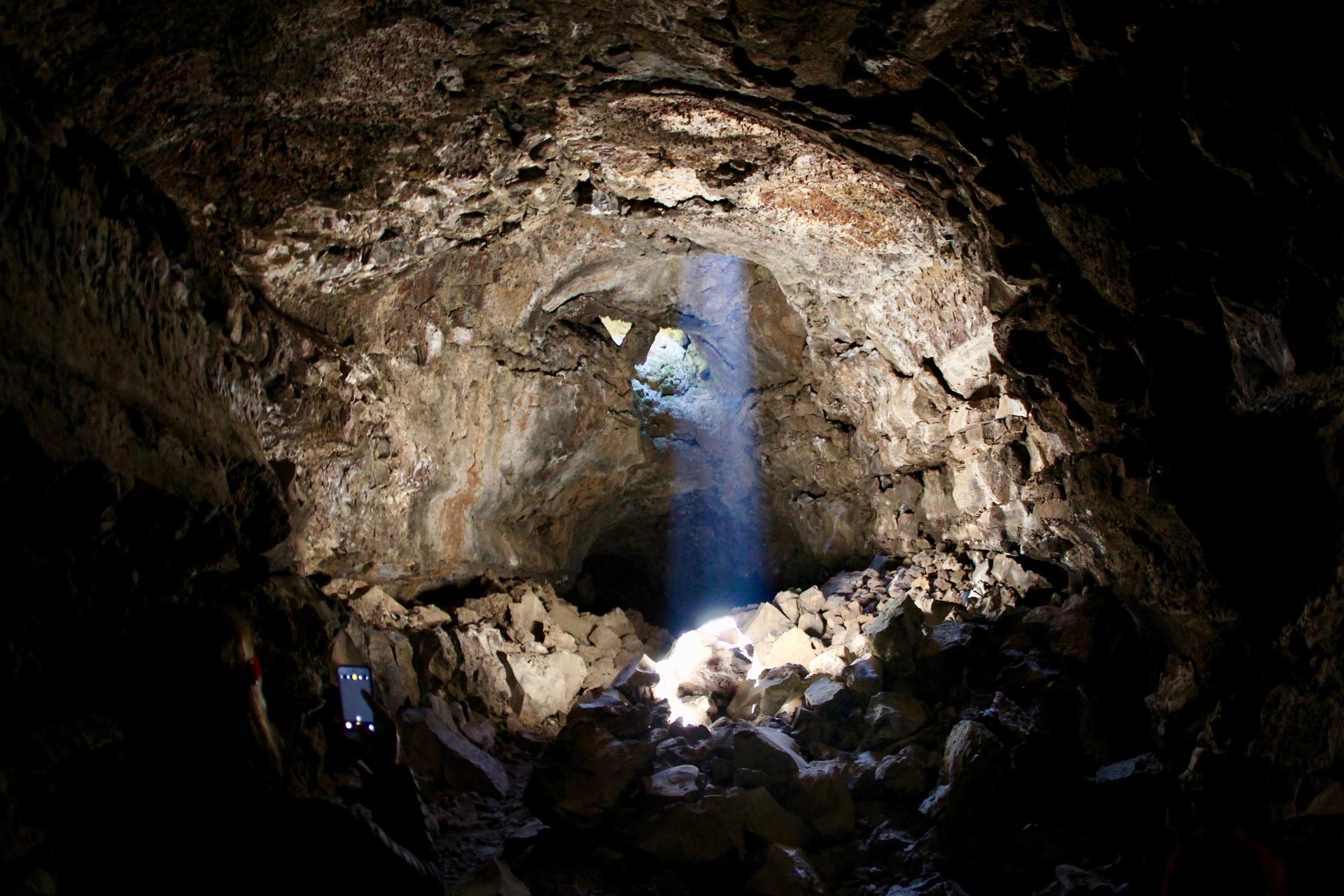 Dark cave interior with a bright beam of light shining through an opening.