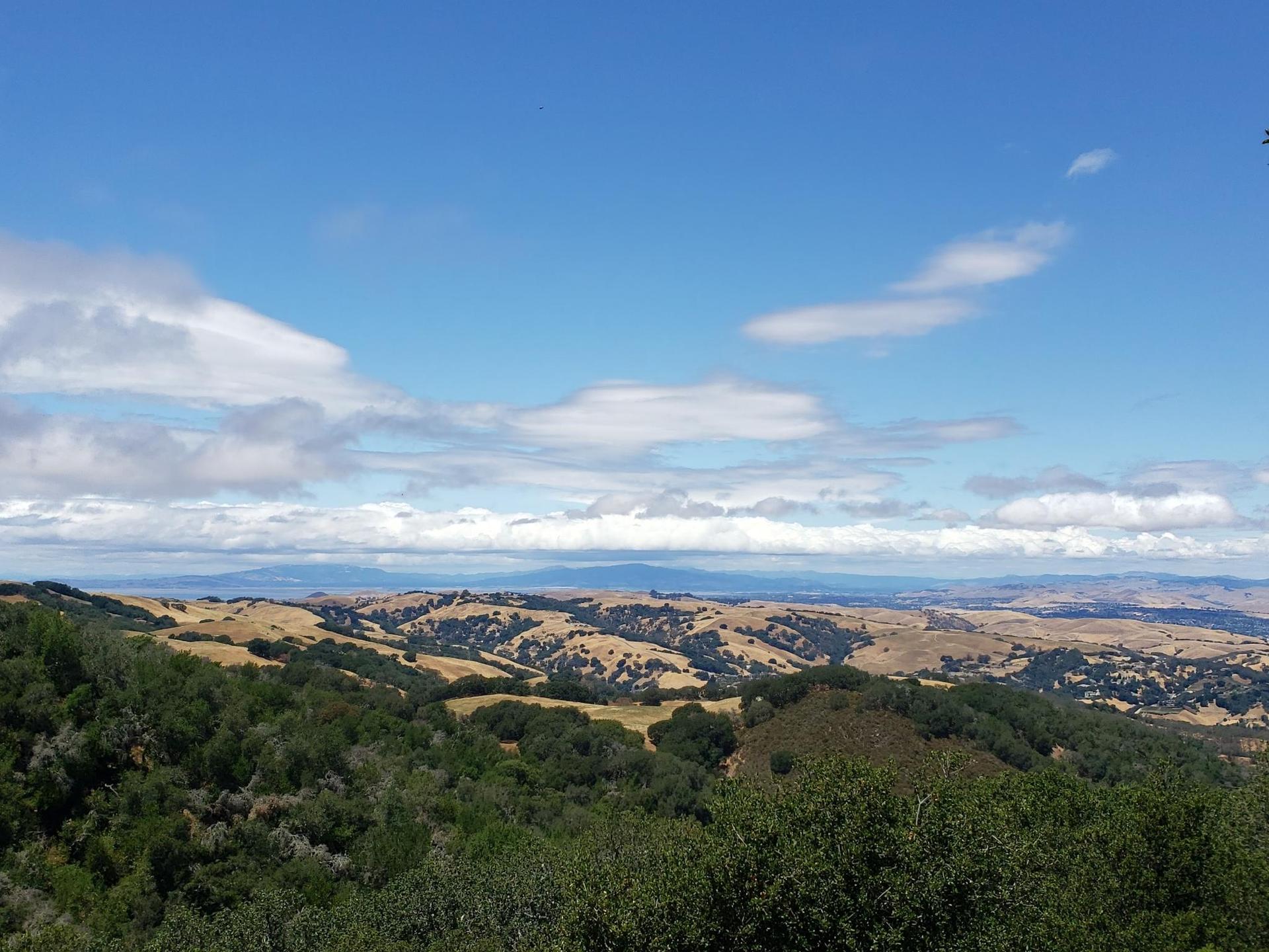 Expansive view of green and golden rolling hills under a partly cloudy sky.