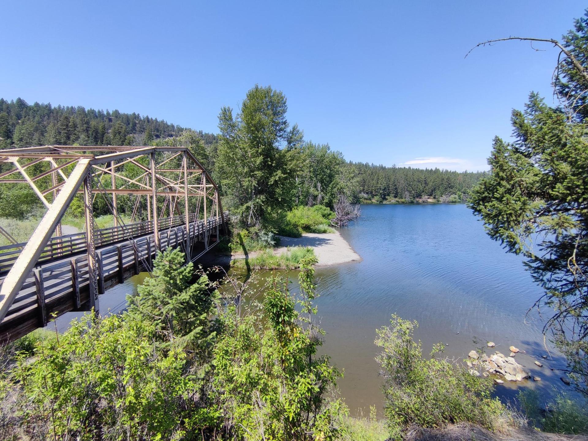 An old metal truss bridge spanning over a calm body of water, surrounded by trees.