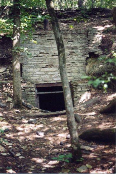 A dark stone structure entrance built into a forested hillside with dappled light.