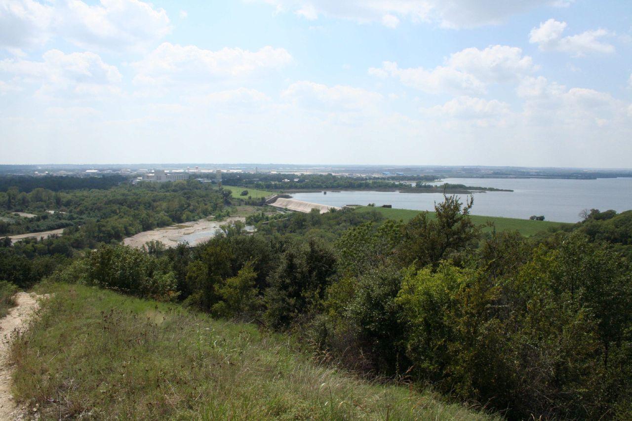Panoramic view of a large lake surrounded by green trees under a cloudy sky.