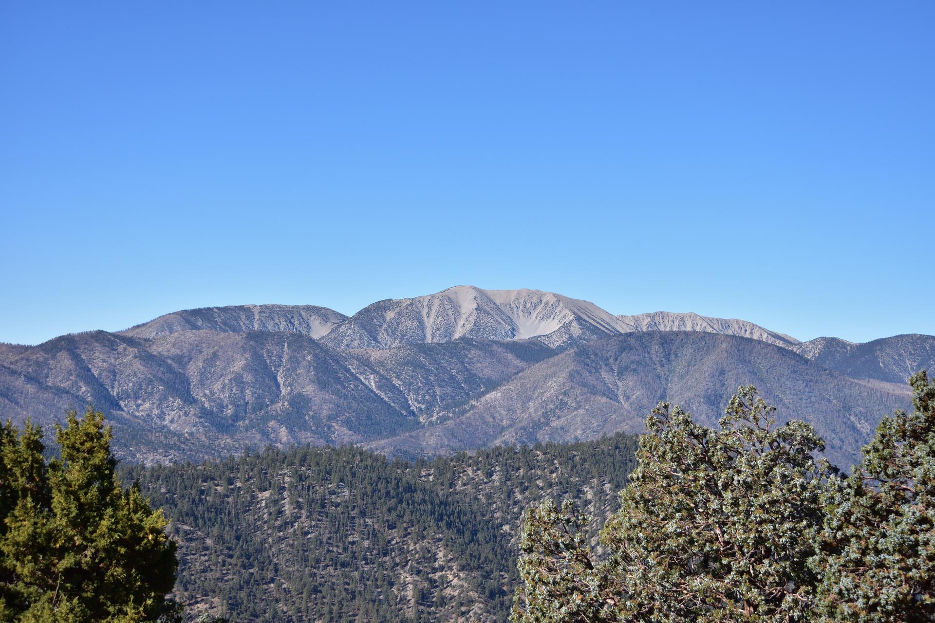 Majestic, sunlit mountains rise above a forested valley under a clear blue sky.