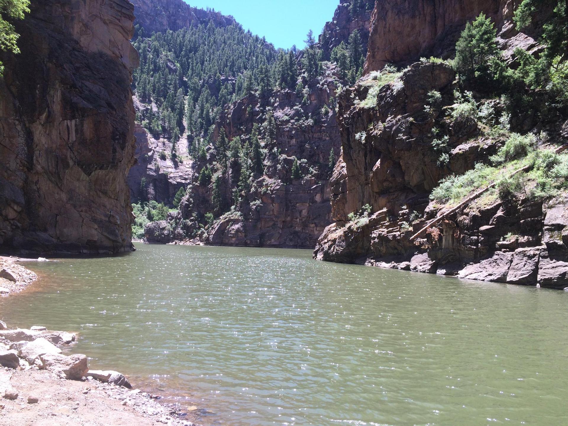 A calm river flowing between tall, rocky canyon walls under a bright sky.