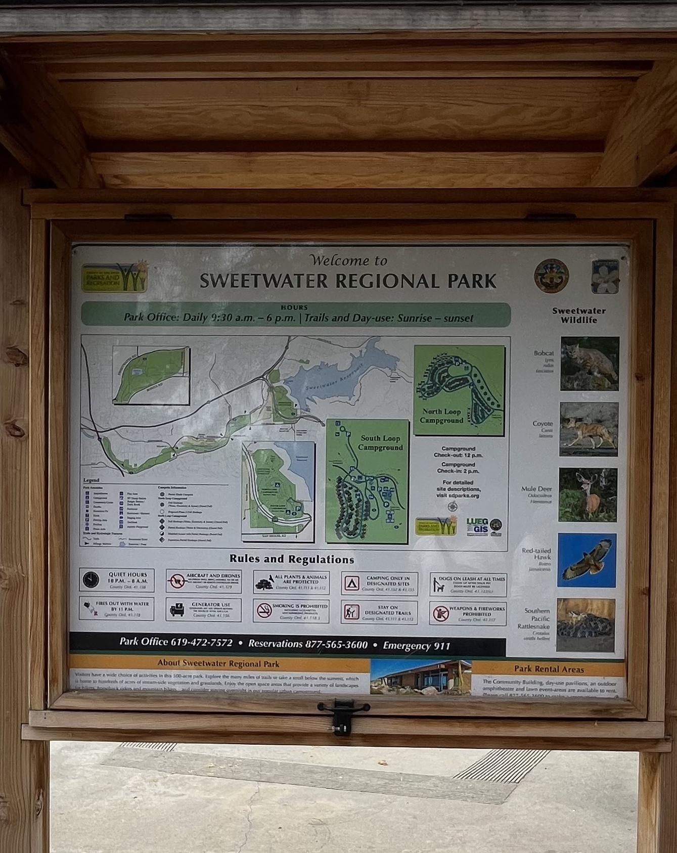 A wooden framed information board with maps, rules, and wildlife photos.