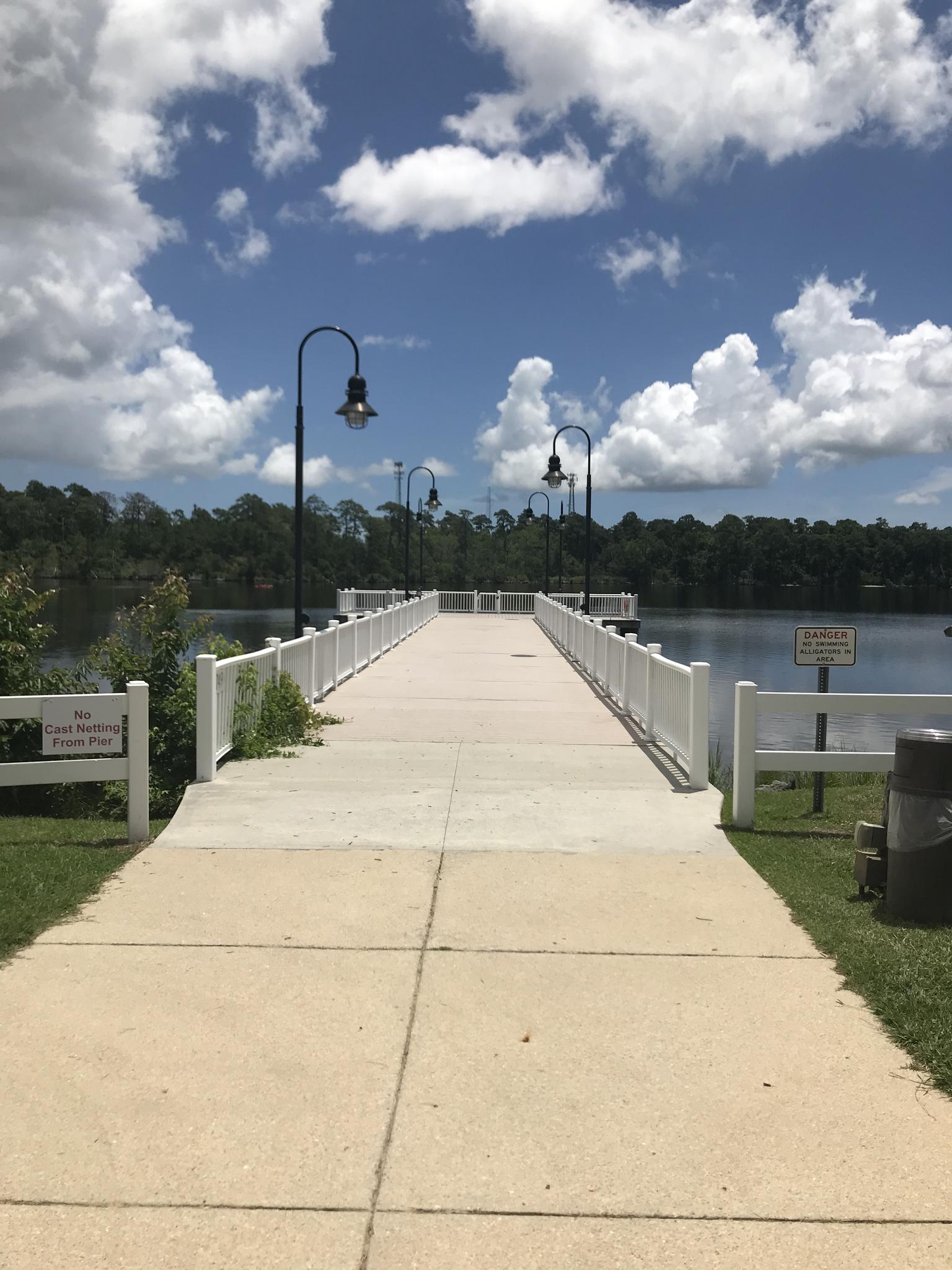 Long white pier with lampposts extending over calm water.