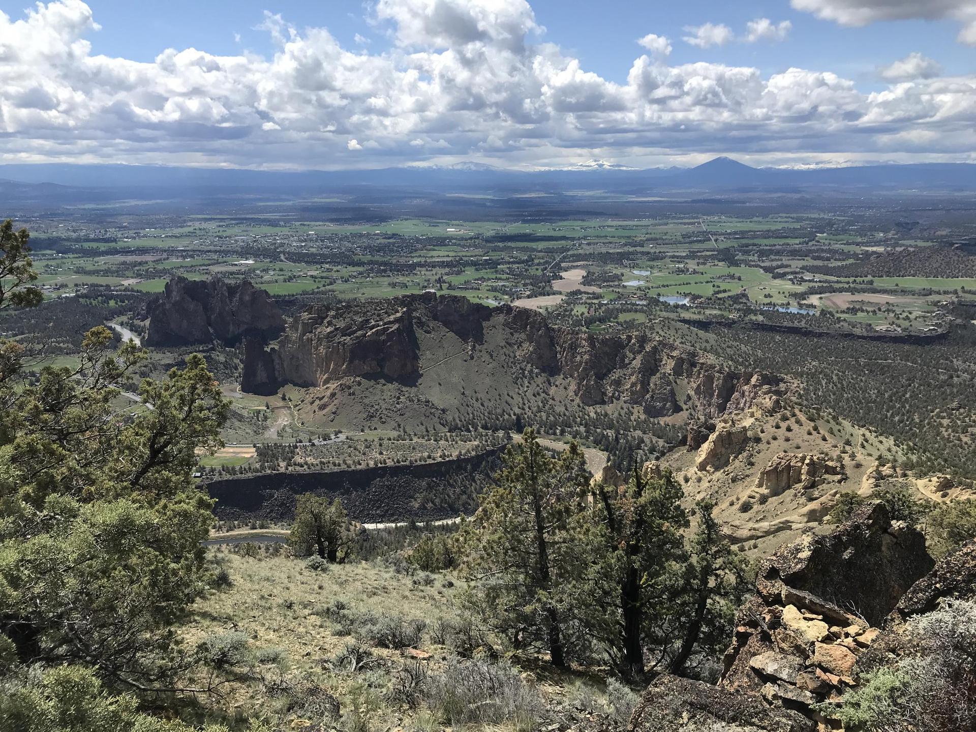 Panoramic view of rocky cliffs, a river, and a green valley under cloudy skies.