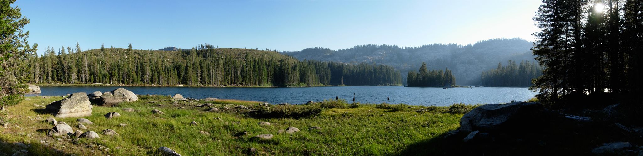 Panoramic view of a calm lake surrounded by dense forests under a bright sky. - Silver Lake to Spanish Peak Trail