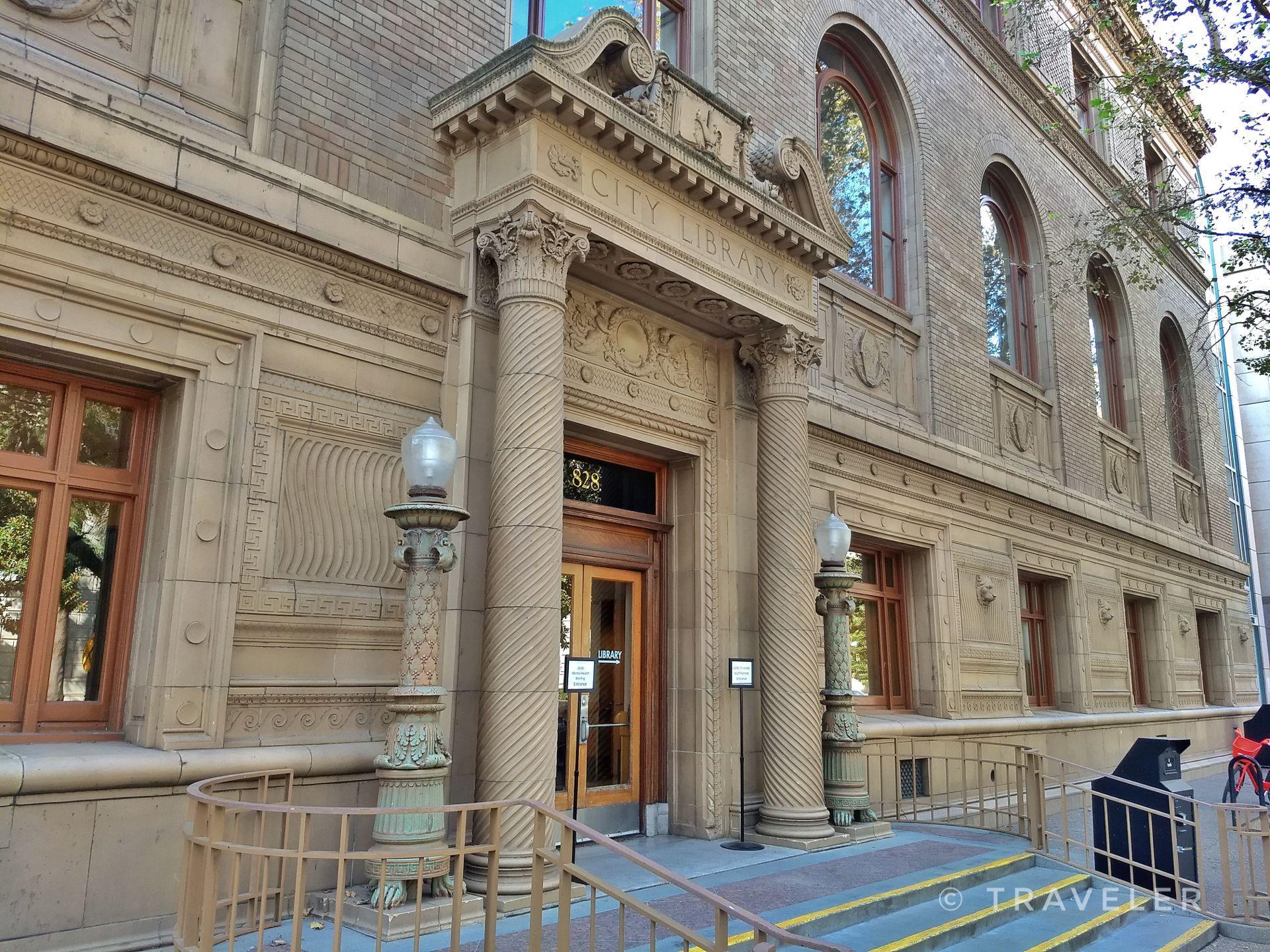 Ornate stone building entrance with columns, lampposts, and steps.