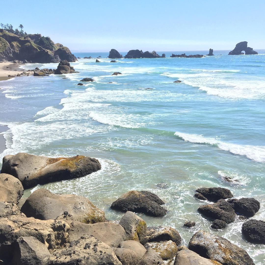 Bright sunny beach with blue water, white waves, and large rocks.