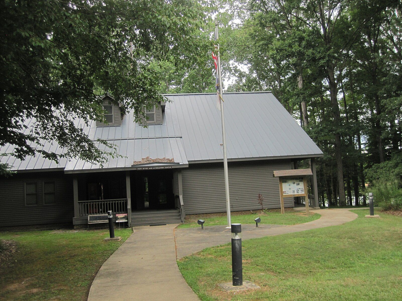 A gray building with a metal roof and flagpole, surrounded by trees. - Falls Lake Trail